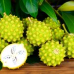 Fresh soursop fruits on a table with tropical leaves.